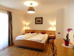 Ein Hotelzimmer mit einem hölzernen Bett, zwei Nachttischlampen, einer Deckenleuchte, einem gerahmten Bild an der Wand und einem Tisch mit einer Topfpflanze.