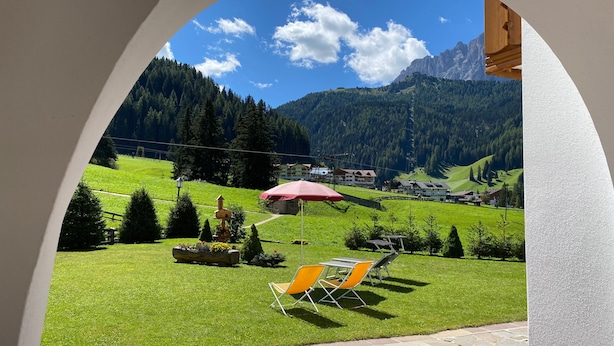 A patio with outdoor furniture, a red umbrella, and a view of a mountainous landscape. - Apartment 'Residence Katiuscia 5' with Mountain View, Private Garden and Wi-Fi (Selva di Val Gardena)