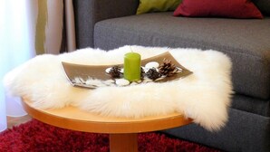 A grey sofa with two pillows, a small round table with a white furry rug, and a candle. - Apartment 'Residence Katiuscia 5' with Mountain View, Private Garden and Wi-Fi (Selva di Val Gardena)