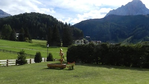 A grassy area with a wooden fence, a birdhouse, and a bench. - Apartment 'Residence Katiuscia 5' with Mountain View, Private Garden and Wi-Fi (Selva di Val Gardena)