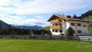 A two-story building with balconies, a mountain backdrop, and a clear sky. - Apartment 'Residence Katiuscia 5' with Mountain View, Private Garden and Wi-Fi (Selva di Val Gardena)