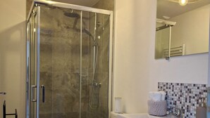 Une salle de bain moderne avec une douche à parois de verre, des toilettes, un meuble-lavabo avec un miroir et un pare-éclaboussures carrelé.