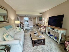 Een woonkamer met een bank, salontafel, televisie en een eethoek met stoelen en een tafel.