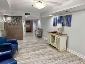Un hall de hotel con suelo de madera, sillas azules, un armario blanco y un pasillo que conduce a una puerta.