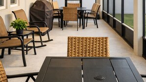 En täckt uteplats med ett bord och stolar, stora fönster och ljusslingor.