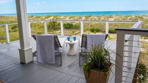 Een overdekt terras met twee stoelen en een tafel, met uitzicht op het strand.