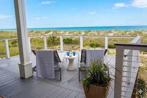 Ein überdachter Außenbereich mit zwei Stühlen und einem Tisch, mit Blick auf einen Strand.