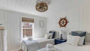 Een kamer met twee bedden, een houten scheepsschijf, een raam met blinds, een rieten dressoir en een kroonluchter.