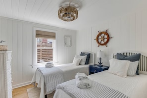 Ein Zimmer mit zwei Betten, ein hölzernes Steuerrad, ein Fenster mit Jalousien, ein Korbuschrank und eine Chandelüster.