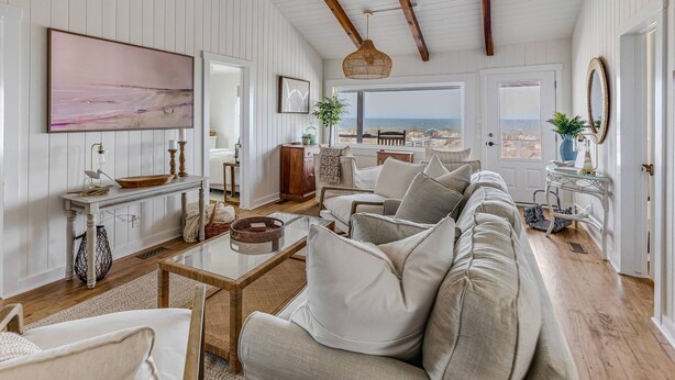 Een ruime woonkamer met een groot raam, een houten plafond en uitzicht op de oceaan.