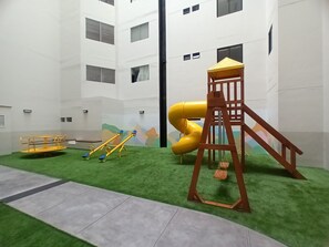 Een speelruimte voor kinderen met een glijbaan, schommel en klimconstructie.