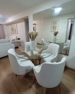 A modern living room with a glass-top coffee table, white sofas, and a large mirror reflecting the room.