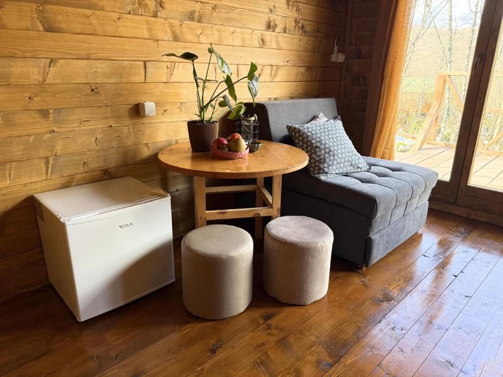 A cozy room with a wooden wall, a sofa, a small round table with cushions, and a Tesla charging station.