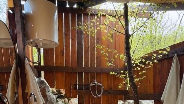 Una terrassa de fusta amb una font de pedra, un suport per tovalloles i una taula de fusta amb bols i espelmes.