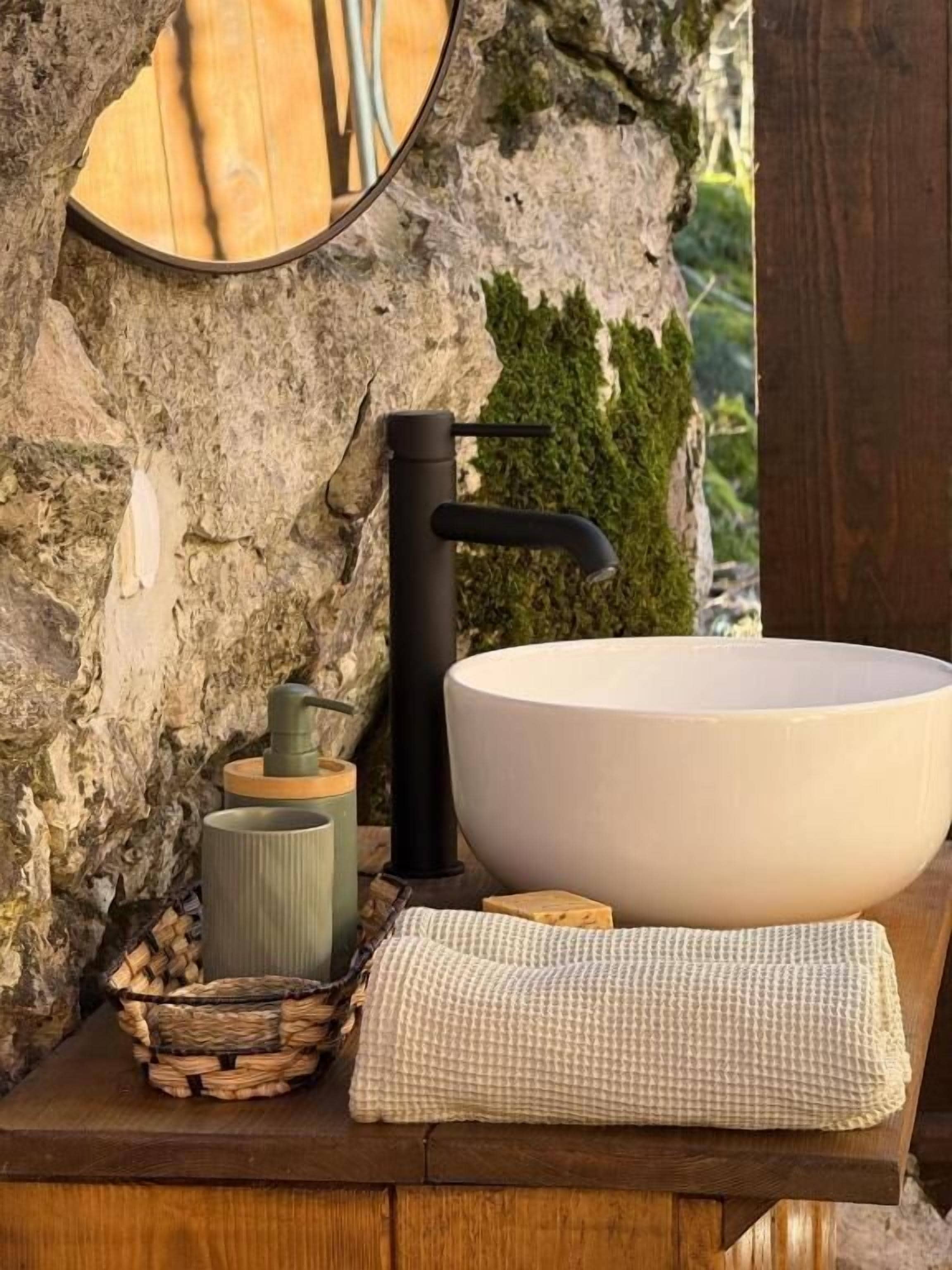 A bathroom with a large white basin, a black faucet, a mirror, a soap dispenser, and a towel on a wooden surface.