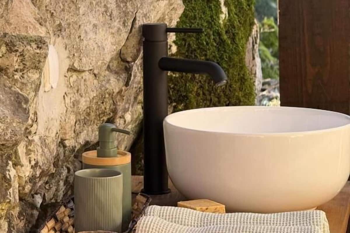 A bathroom with a large white basin, a black faucet, a mirror, a soap dispenser, and a towel on a wooden surface.