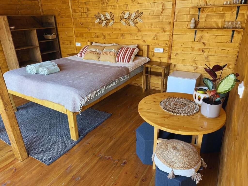Een houten kamer met een bed, een klein tafeltje en een plank met spullen.