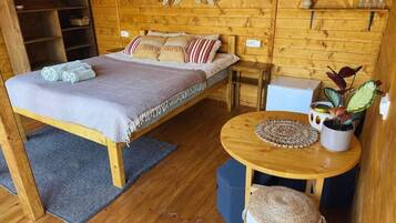 Een houten kamer met een bed, een klein tafeltje en een plank met spullen.