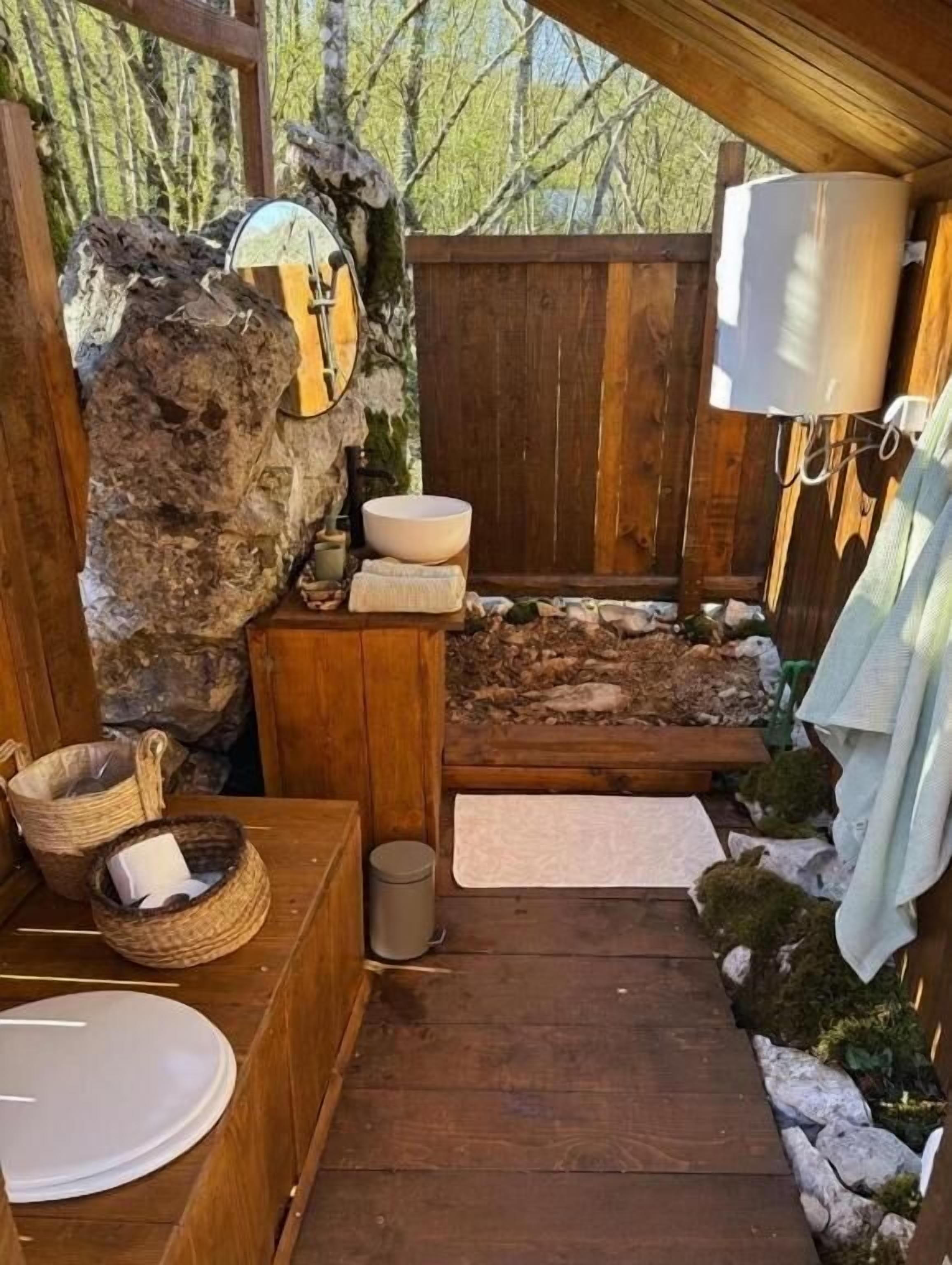 A rustic bathroom with a wooden floor, a stone wall, a wooden bench, a sink, and a mirror.