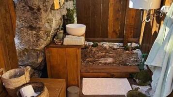 A rustic bathroom with a wooden floor, a stone wall, a wooden bench, a sink, and a mirror.
