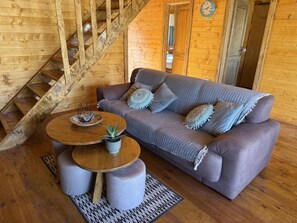 A wooden interior with a sofa, ottomans, a round table, and a staircase. - Wilgano (Rvaši)