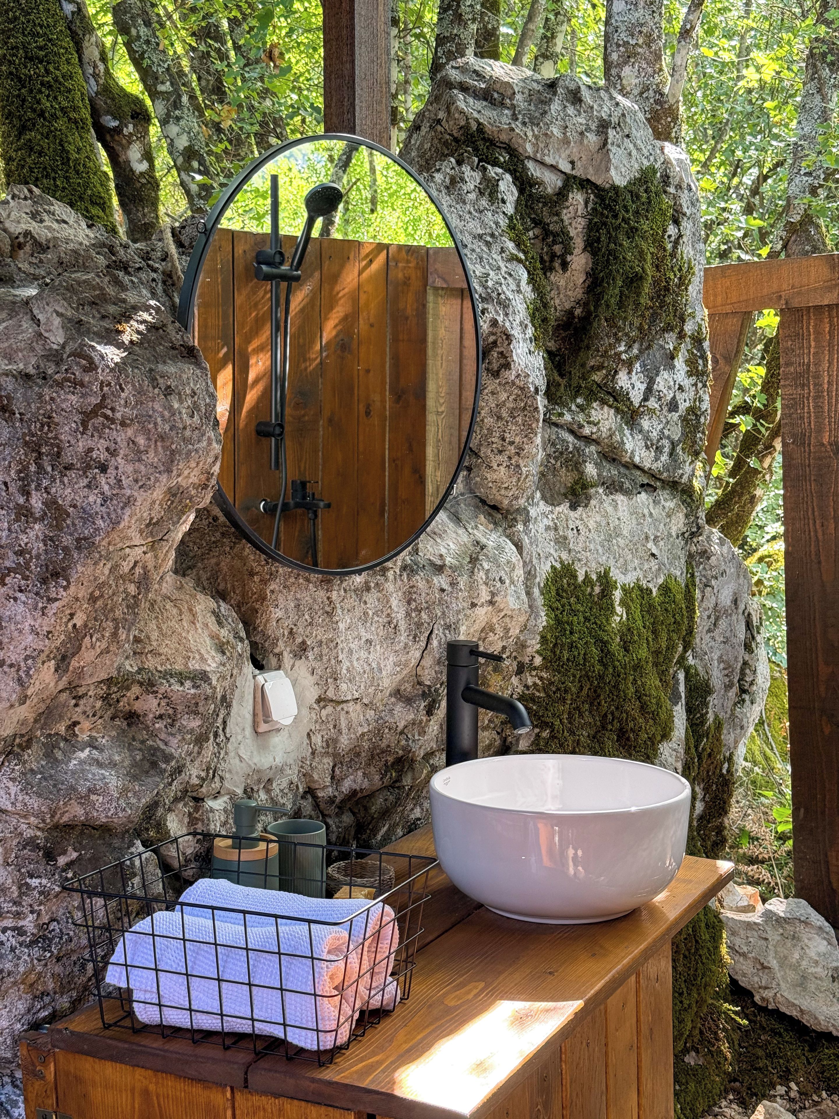 Un baño rústico con un tocador de madera, un lavabo blanco grande, un espejo redondo y un grifo negro.