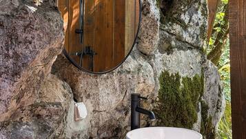 Un baño rústico con un tocador de madera, un lavabo blanco grande, un espejo redondo y un grifo negro.