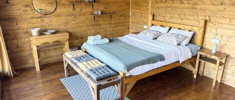 A wooden cabin bedroom with a bed, bedside tables, a mirror, and a clock.