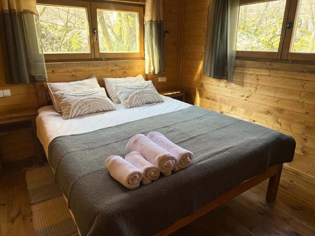 Quarto de cabana de madeira com cama, travesseiros e toalhas enroladas.