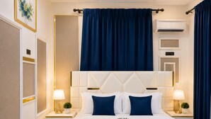 Camera d'albergo con un letto grande, due comodini con lampade, un condizionatore fissato al muro e una tenda blu.