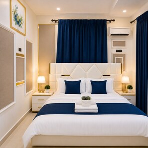 Ein Hotelzimmer mit einem großen Bett, zwei Nachttischen mit Lampen, einer Wand-Klimaanlage und einem blauen Vorhang.