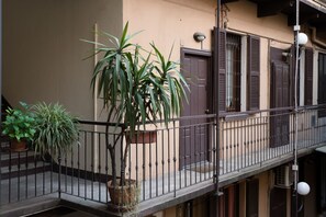 A balcony with a potted plant, a railing, and a building facade with shutters. - Procaccini, 54 – Urban Stay Sempione–Sarpi (Milano)