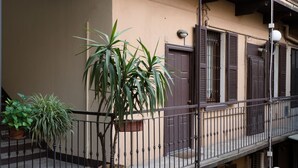 Ein Balkon mit einer Topfpflanze, einem Geländer und einer Gebäudefassade mit Fensterläden.