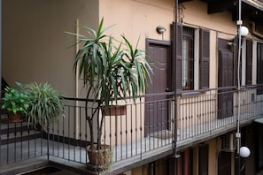 A balcony with a potted plant, a railing, and a building facade with shutters. - Procaccini, 54 – Urban Stay Sempione–Sarpi (Milano)