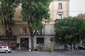 Straßenansicht mit einem Gebäude, das einen geschlossenen Laden, einen Baum und geparkte Autos zeigt.