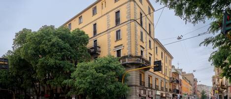 A multi-story building with balconies, parked cars, and trees along the street.
