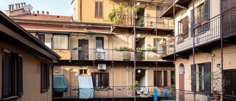Un edificio residencial de varios pisos con balcones, aire acondicionado y plantas en macetas.