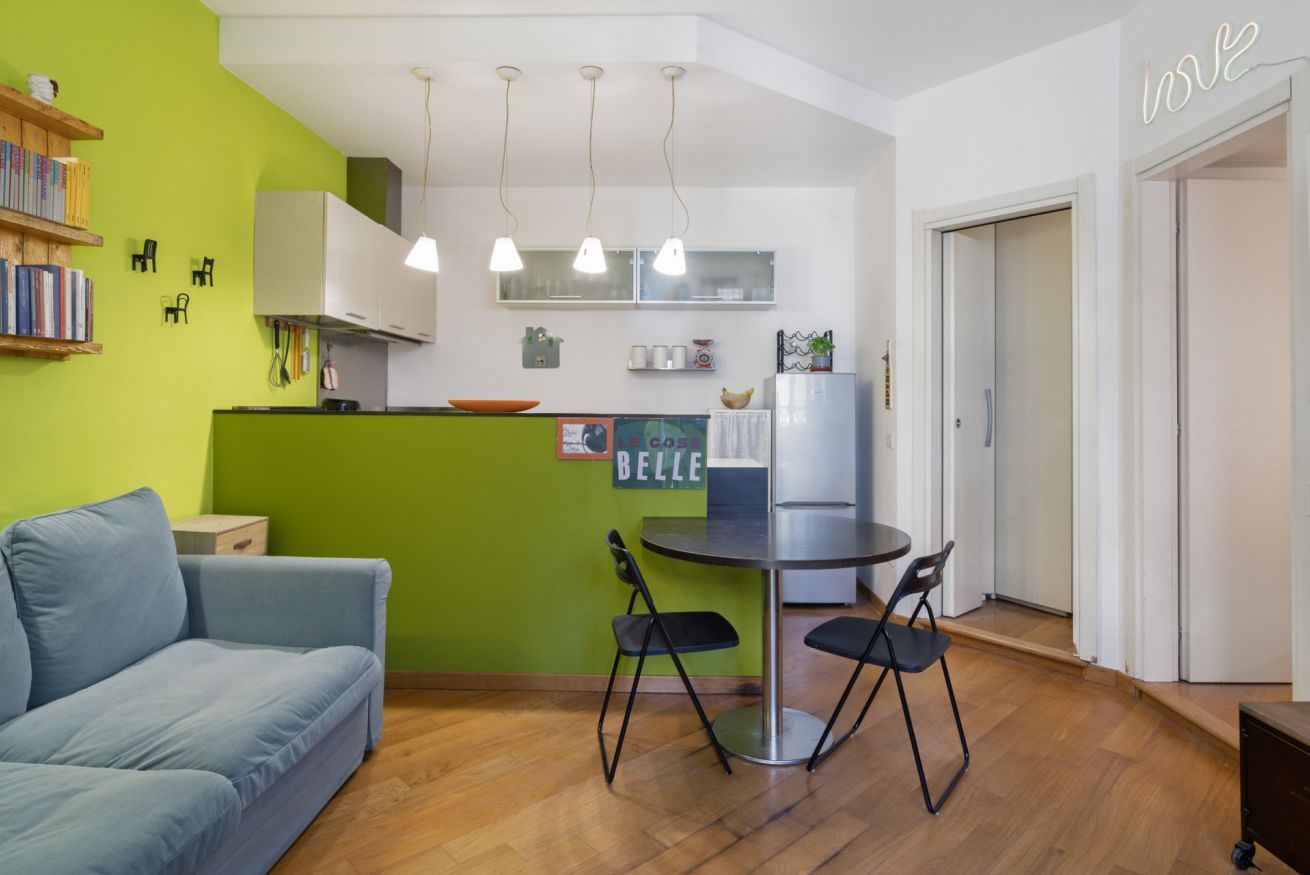 Ein kompakter Wohnraum mit einer Küchenzeile, einem Essbereich mit Tisch und Stühlen, einer Couch und einer Neonreklame.