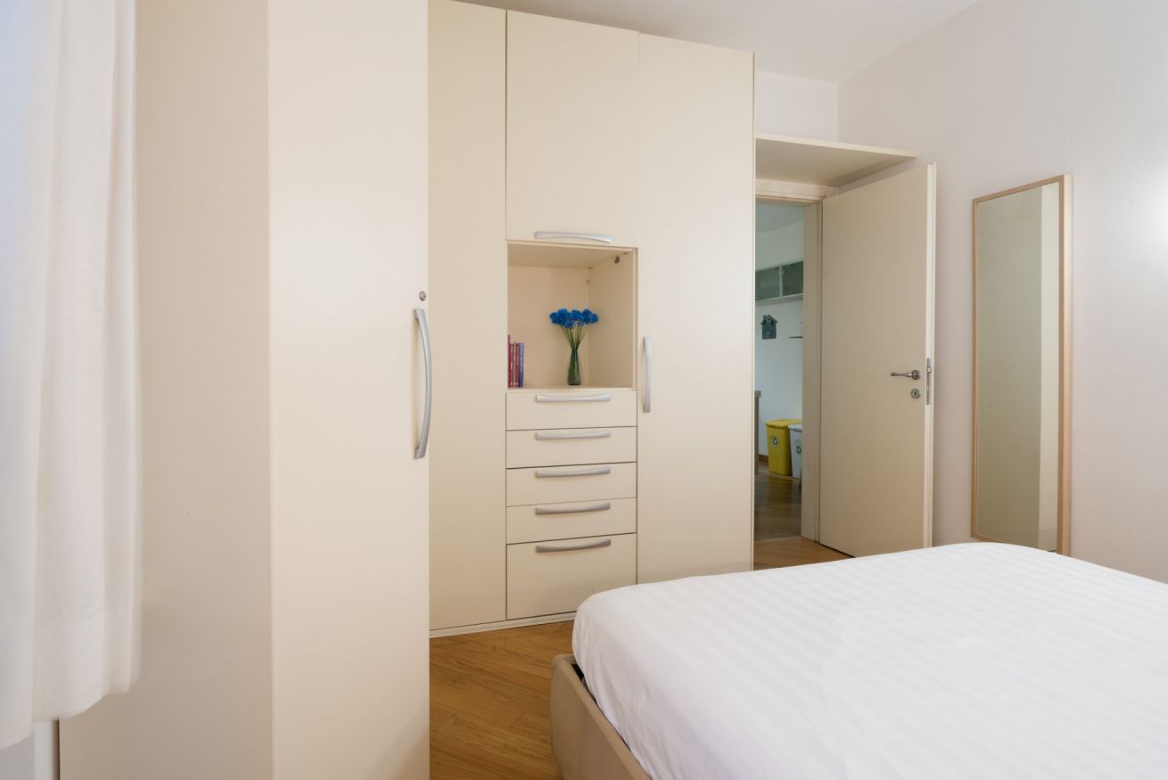 A bedroom with a bed, a wardrobe, and a small shelf with a vase.