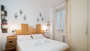 Ein ordentlich eingerichtetes Schlafzimmer mit einem hölzernen Kopfteil, einem Nachttisch mit Lampe, einem Kleiderschrank und einem Fenster mit Vorhängen.