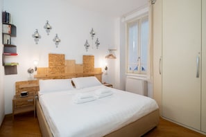 A neatly arranged bedroom with a wooden headboard, a bedside table with a lamp, a wardrobe, and a window with curtains. - Procaccini, 54 – Urban Stay Sempione–Sarpi (Milano)
