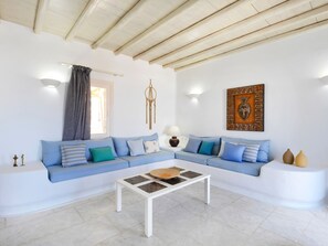 A modern living room with a blue sofa, a white coffee table, and a decorative wall piece. - Parfait Luxury Villa Mykonos | Private Pool & Aegean Sea Views (Mykonos)