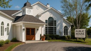 A white public house with a prominent bell tower, a large arched window, and a sign indicating its location in North Creek.