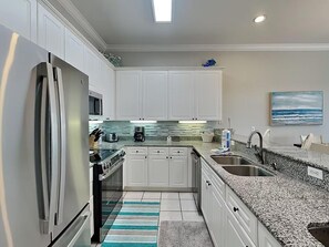 A modern kitchen with white cabinets, a granite countertop, stainless steel appliances, and a striped rug. - Seascape Golf Villas 407 (Miramar Beach)