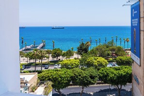 Un paysage urbain côtier avec vue sur la mer, une jetée et un parking avec des voitures et des arbres.