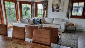 A modern living room with a large wooden dining table, a sofa set, and a view of greenery through large windows. - Boekhorst Royal 6 (Susteren)