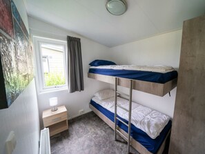 Een slaapkamer met een stapelbed, raam, nachtkastje en radiator.