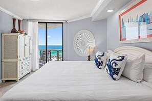 A bedroom with a large bed, a dresser, a round wall decoration, and a view of the ocean. - Surfside Resort #604 (Miramar Beach)