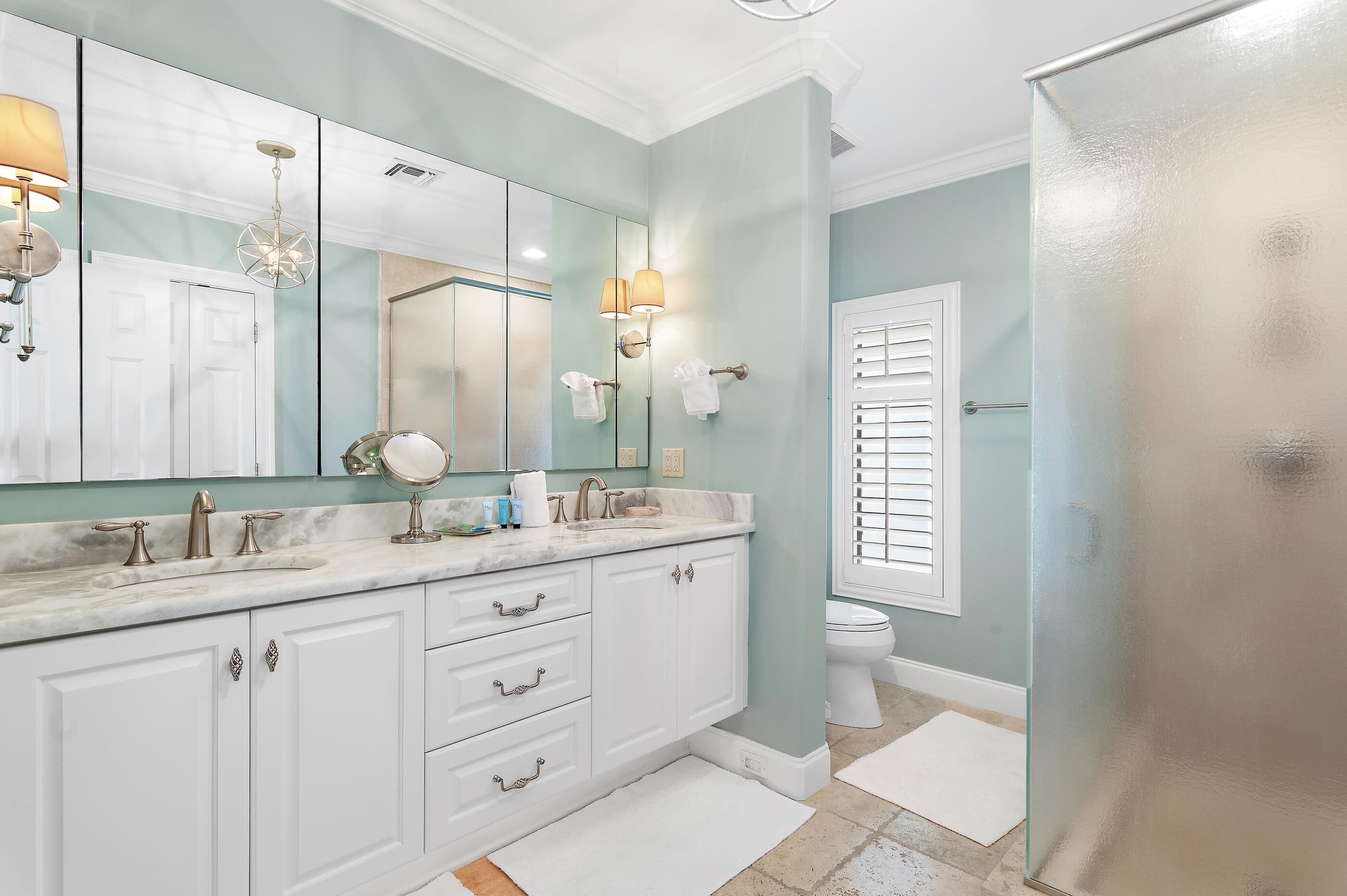 A bathroom with a large mirror, white cabinets, a marble countertop, and a glass shower enclosure.