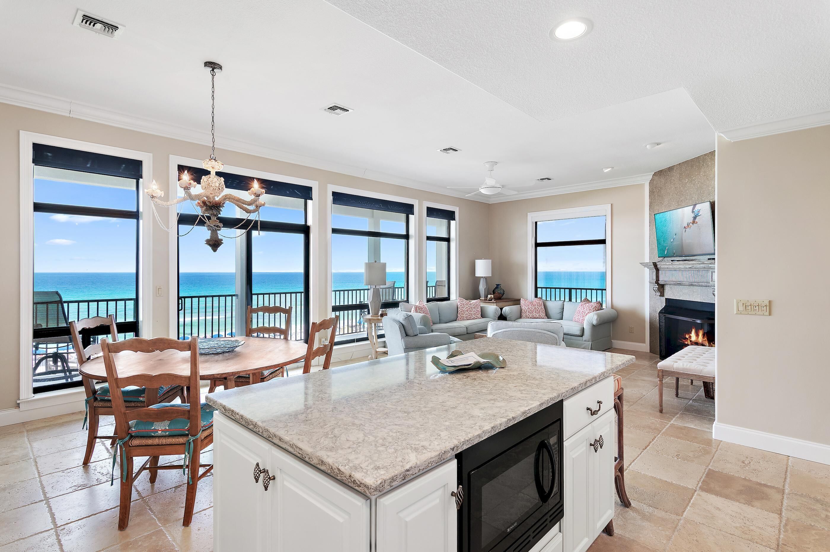 A spacious living area with a large window overlooking the ocean, a fireplace, and a kitchen with a central island.